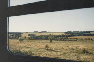 Rolling countryside and distant tree line framed by the train window