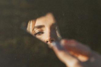 A hand holds a piece of cracked mirror with warm light illuminating the fingers