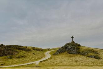Hilltop cross rising above rolling grasslands beneath an overcast sky