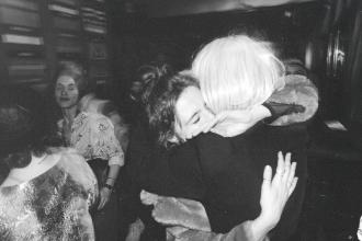 Candid moment of two individuals hugging in a busy room with soft lighting