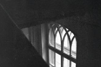 A softly lit arched window seen from above in a dark interior, with faint light shining through the glass panes