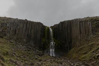 Tall waterfall cascading through a narrow gap between vertical basalt rock columns