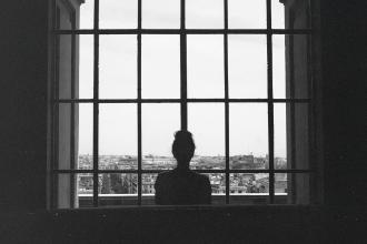 Silhouetted figure stands before a large grid‑paneled window, looking out over a sprawling cityscape