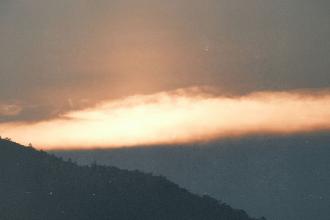 A glowing band of orange light spreads across the horizon at sunset, illuminating the sky above the dark silhouette of a mountain ridge