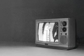 Vintage television sits in a dim room, displaying a black‑and‑white image of tall buildings framed by palm leaves