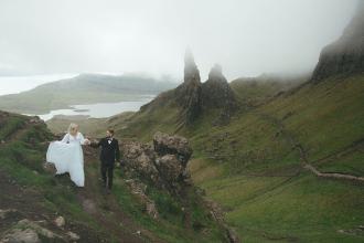 ride and groom holding hands while hiking through mist-covered highlands with steep cliffs and rolling green hills