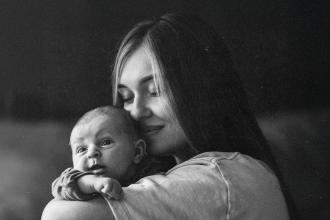 Woman holds a small baby close against her shoulder in a quiet, softly lit setting