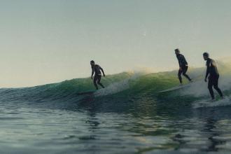 Three surfers ride a green ocean wave together in the soft light of early morning or late afternoon