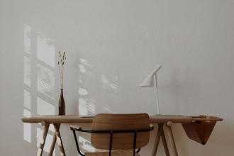 andinavian-style workspace featuring a wooden desk, simple chair, white lamp, and dried botanicals with sunlight filtering through a nearby window