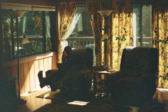 Cozy living room with patterned curtains and large windows, where someone sits in a recliner next to soft natural light
