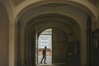A person walks through a large arched doorway into a quiet courtyard, framed by the tall curved entryway