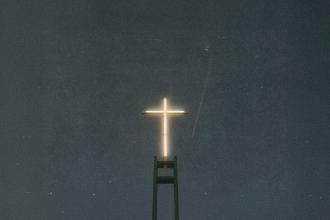 A glowing cross sits atop a tall structure against a dark, starless night sky