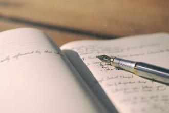 A fountain pen rests on the open pages of a notebook filled with handwritten notes, lit by warm natural light