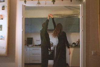 Two people dance together in a warmly lit kitchen, holding hands as they spin between the doorway and the counter