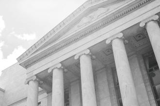 A stone building with tall columns and classical architecture is shown from a low angle, emphasizing its height and symmetry