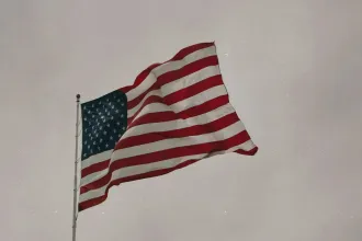 An American flag waves on a tall flagpole against a muted, overcast sky