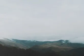 A series of low, rolling mountains are partially covered in mist beneath a gray, overcast sky