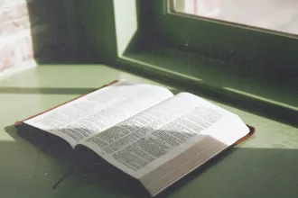 An open Bible rests on a windowsill, lit by soft natural light streaming through a nearby window