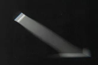 A narrow beam of light shines through a small window or opening, cutting across a dark room and illuminating a portion of the wall and floor