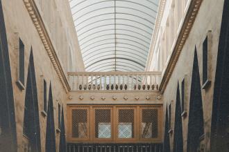 A long interior hallway with tall walls, arched glass ceiling, and symmetrical architectural details