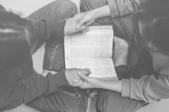 Two people sitting cross-legged, holding hands over an open book placed between them