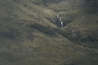 A wide view of rolling hills with a narrow waterfall cascading down the center of the landscape