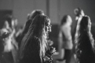 Group of people standing closely together in a dimly lit indoor setting during worship.