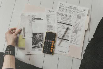 Assorted tax forms and financial papers spread out beside a smartphone calculator and pen