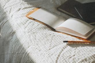 Open notebook resting on a textured blanket beside a pen in warm natural light