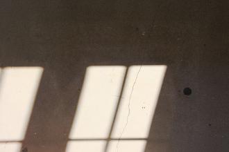 Rectangular window light casting three bright beams onto a textured wall with subtle cracks and shadows