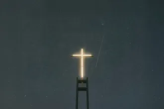 Illuminated cross glowing against a dark night sky atop a tall church structure