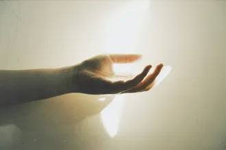 Outstretched hand reaching toward a bright beam of light against a softly lit wall