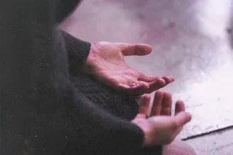 Close-up image of a person's hand resting, palms up, on their lap as they kneel on the floor