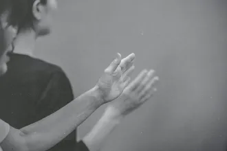 Hands raised in worship or praise during a quiet, reverent moment in a black‑and‑white scene