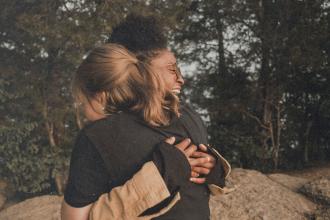 Two people embracing outdoors near large rocks, surrounded by trees and natural scenery