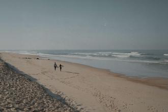 Couple walking along an empty sandy beach beside gentle ocean waves
