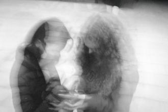 Two people sitting closely together in a soft, double‑exposed black‑and‑white image, creating a dreamy, motion‑blur effect