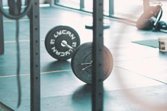 Barbell loaded with weight plates resting on a gym floor in a bright workout space