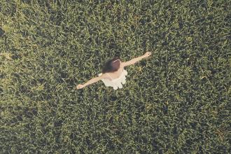 Woman standing with open arms in the middle of a lush green field, viewed from above