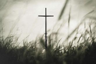 A solitary cross standing in a field of tall grass under a soft, muted sky