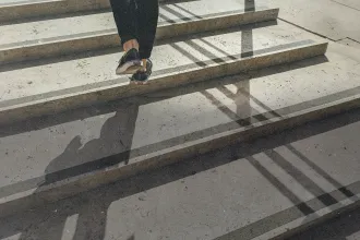 Person walking up concrete steps with sunlight casting long shadows across the staircase