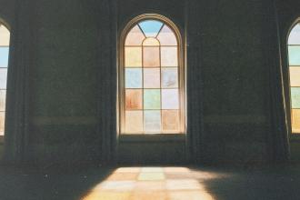 Sunlight shining through tall stained‑glass windows inside a dimly lit room