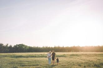 A family walking together through an open grassy field at sunset, holding hands and enjoying the warm light