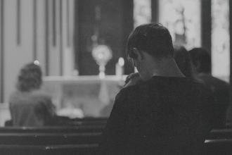 A dimly lit interior of a church where a person sits in a pew facing the altar
