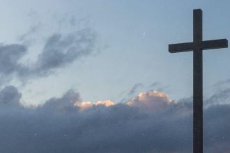 A large cross silhouetted against a cloudy sky with soft light breaking through