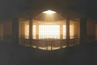 Sunlight streaming through a large skylight and grid-patterned windows, illuminating the upper level of a spacious interior with railings and supporting columns