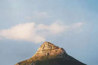 Sunlit rocky mountain peak rising against a soft blue sky with scattered clouds