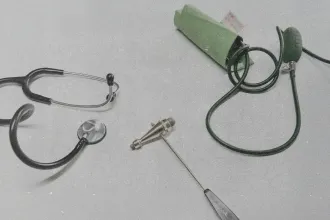 Stethoscope, blood pressure cuff, and reflex hammer arranged on a light surface