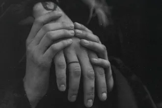 Close‑up of two people gently holding hands in a black‑and‑white scene