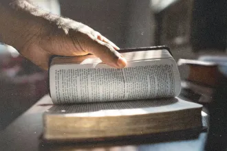 Hand turning a page in an open Bible as sunlight shines across the text